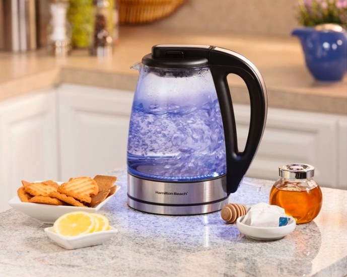 Tea kettle on a counter next to bowl with cookies, lemon, honey and tea bags