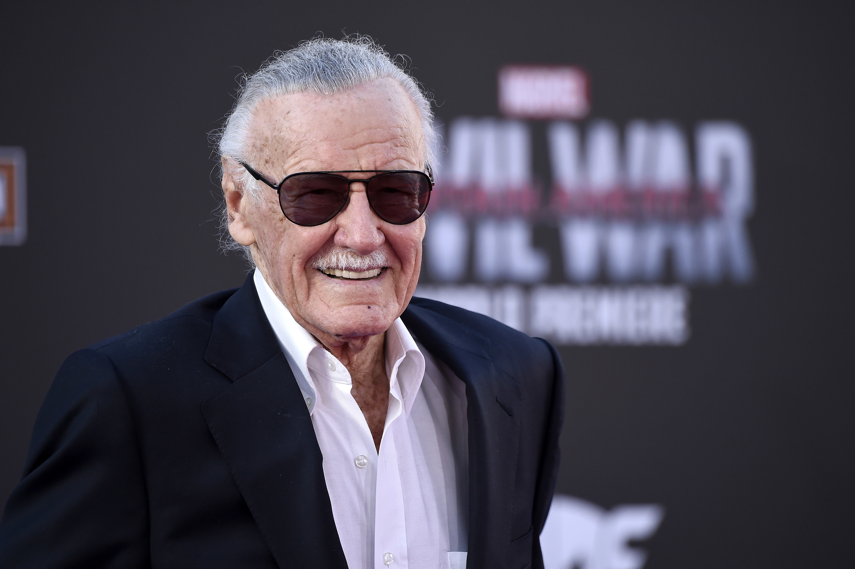 Stan is smiling at the Captain America: Civil War premiere, wearing a black blazer, white shirt and sunglasses