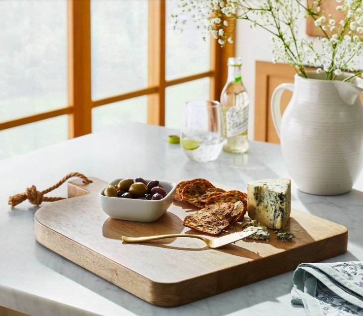 Wood board with cheese, crackers and a bowl of olives