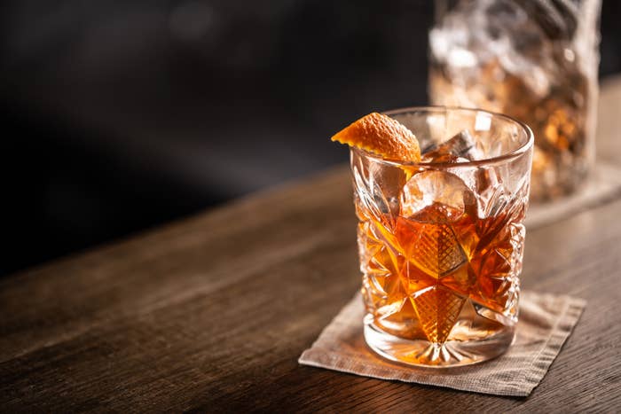 Old-fashioned whiskey drink on ice with orange zest garnish