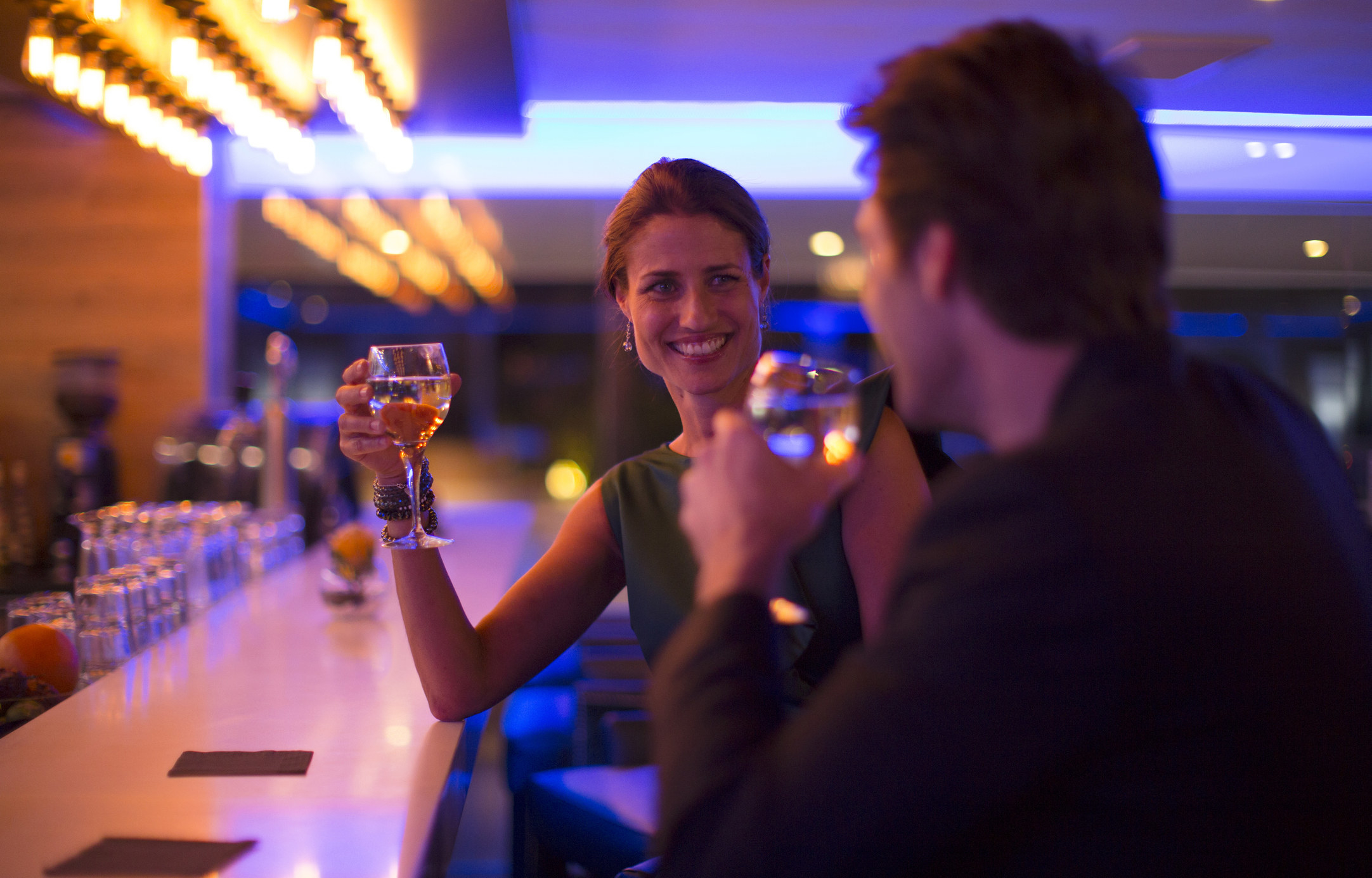A woman and man having a drink and talking at a bar.