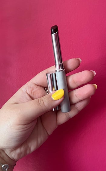 Bianca holding up a tube of the black honey lipstick against a brightly-coloured wall