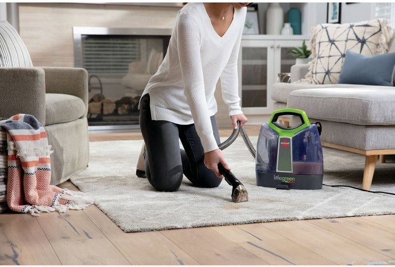 a model on their knees using the carpet cleaner on a rug