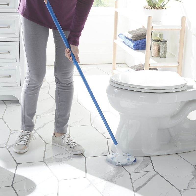 a model using the blue and white scrubber around the base of a toilet