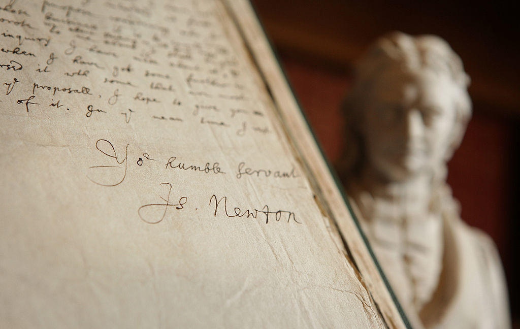 A signature of Isaac Newton contained in a book of his letters is displayed next to a statue of him at the Royal Society on November 24, 2009 in London