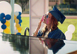 Billie Lourd as Gigi sits at a piano and blows a kiss while wearing a graduation cap and gown in &quot;Booksmart&quot;