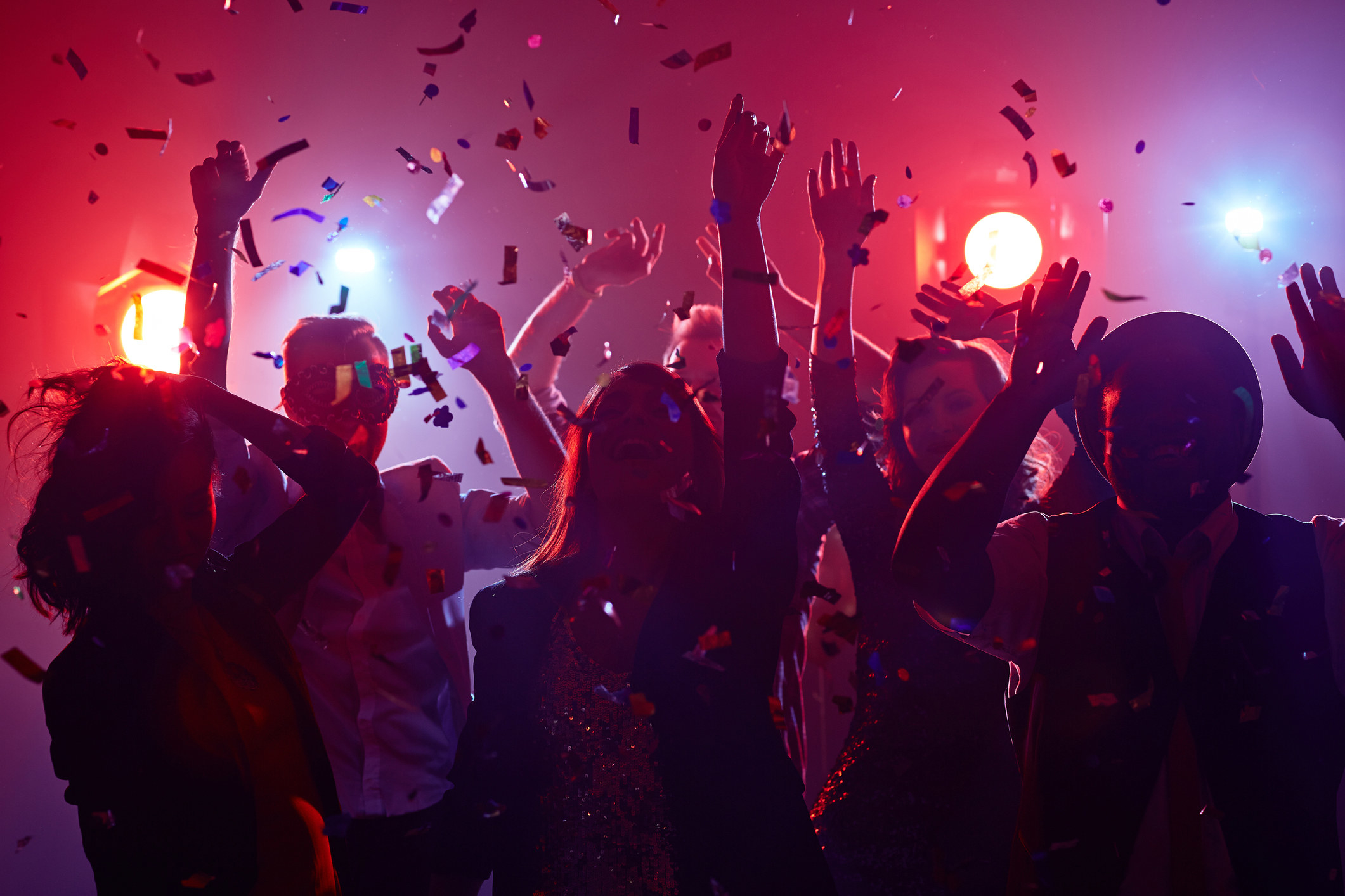 Young people dance in a dark room as confetti rains down on them