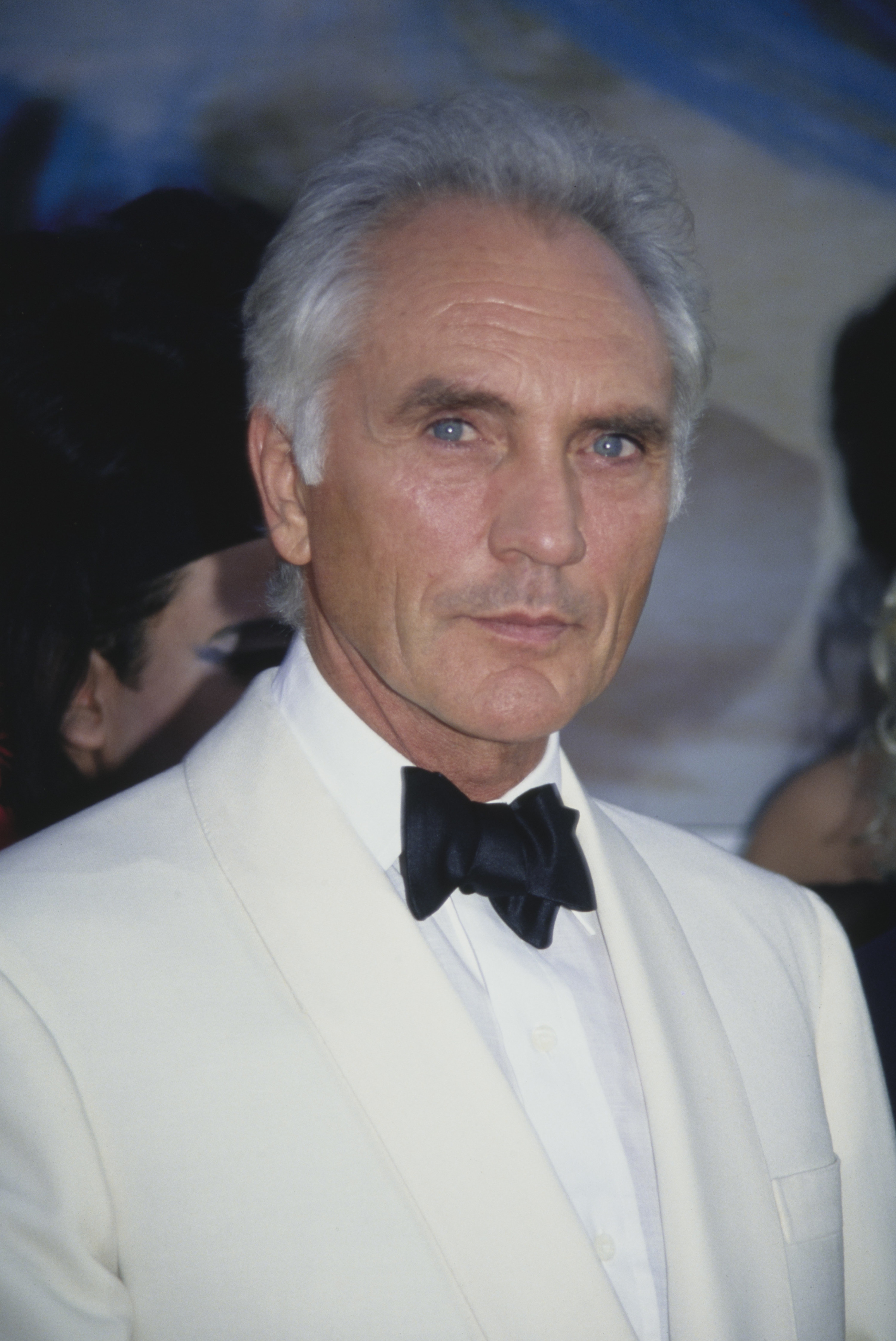 Terrence wearing a white suit with a black bow tie, looking at the camera