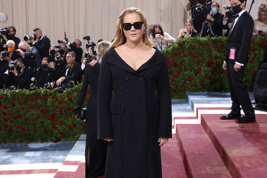 Amy Schumer wearing a simple, long-sleeve black dress and sunglasses