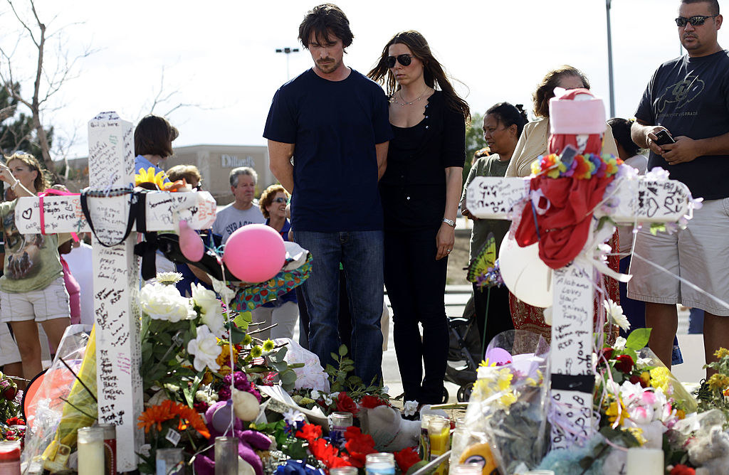 People standing in front of a memorial with flowers, balloons, and large crosses with handwriting on them