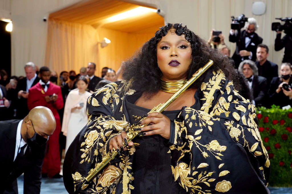 Lizzo in a long, black and gold embellished coat and flute