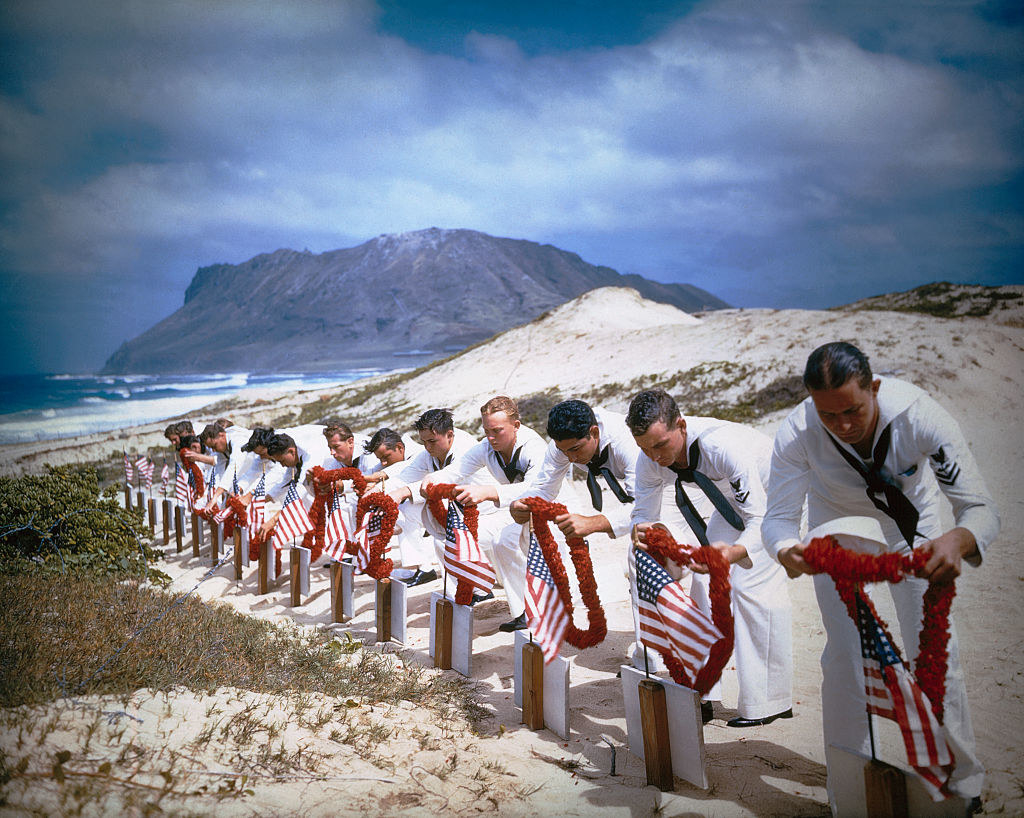 Uniformed US sailors place leis over the graves of their brothers-in-arms along the shore in spring 1942