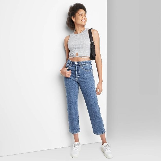 The model wears the cropped blue jeans with a grey tank and white shoes