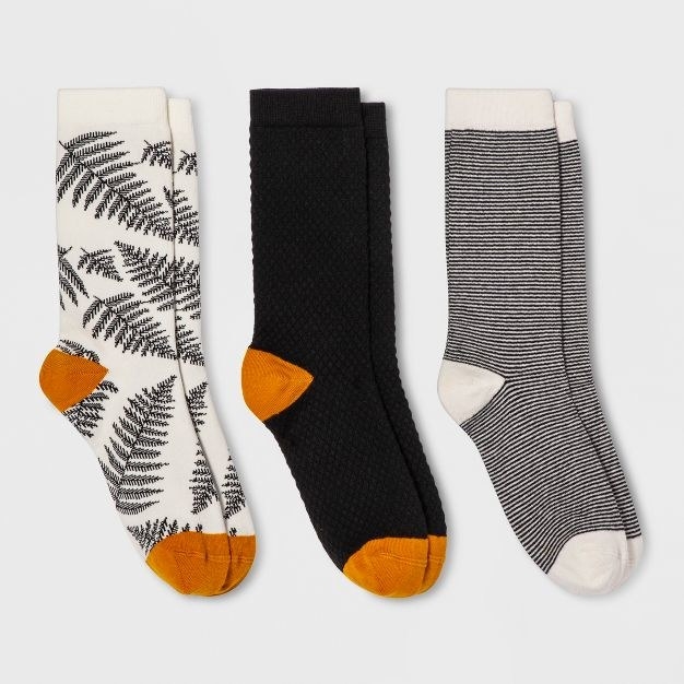 There&#x27;s a white pair with black fern detailing and orange accents, a solid black textured pair with orange accents, and a black and white thin horizontal stripe pair with white accents