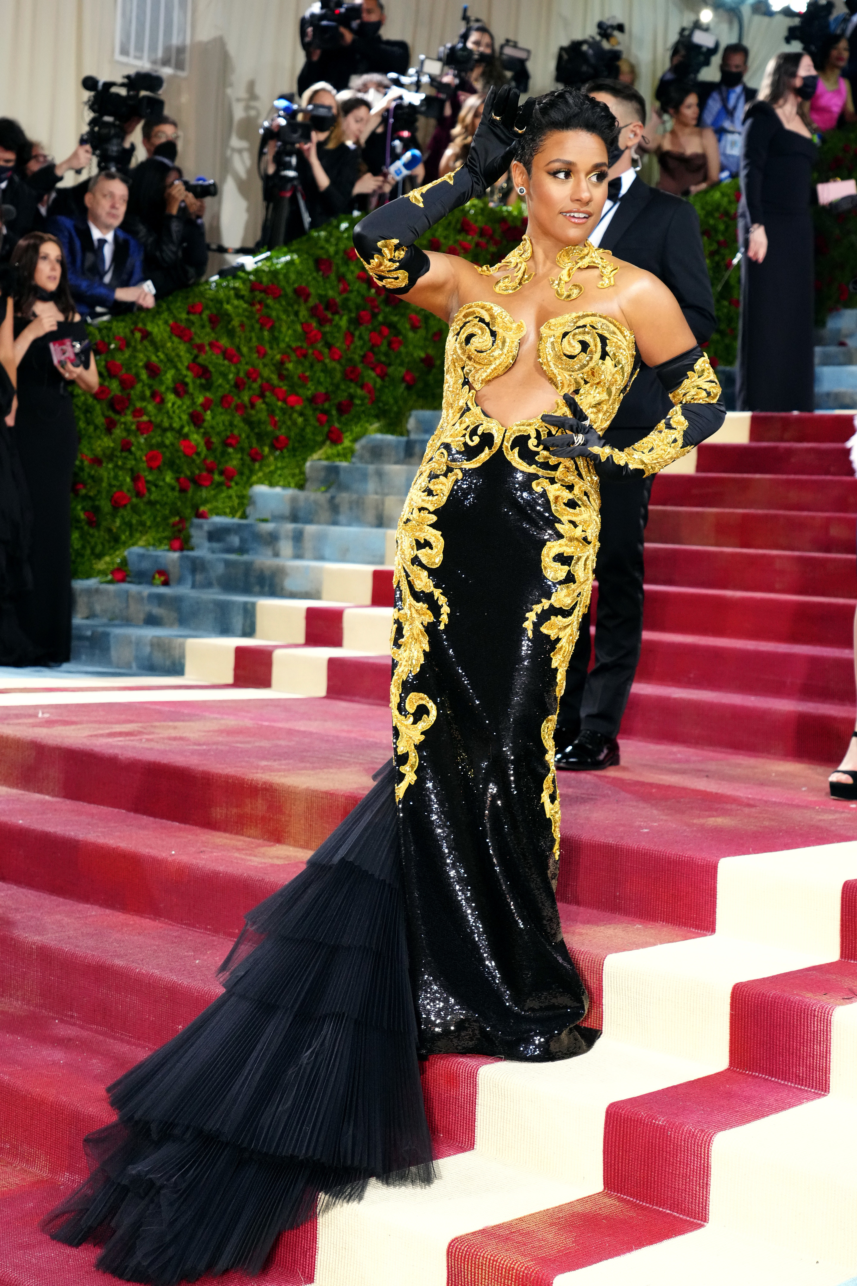 Ariana in a long gown with gold accents, layered train, and matching arm-length gloves