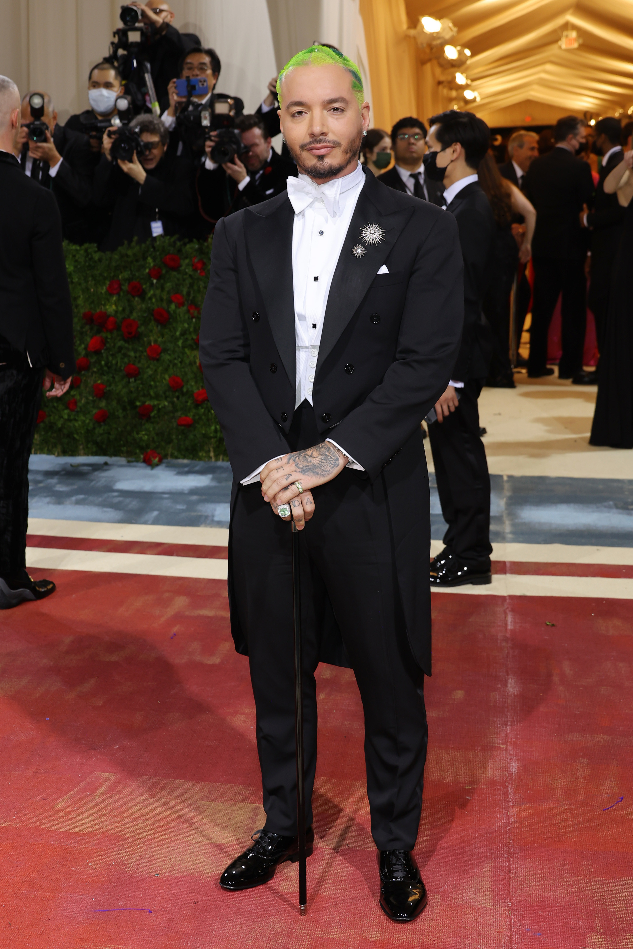 J Balvin in a long tux and bow tie holding a walking stick