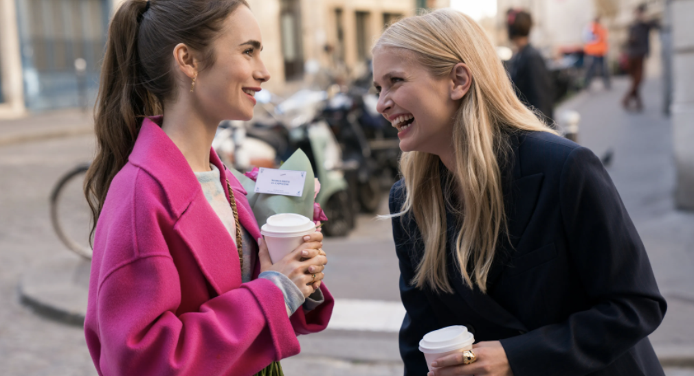 Two women hold cups of coffee and smile while conversing