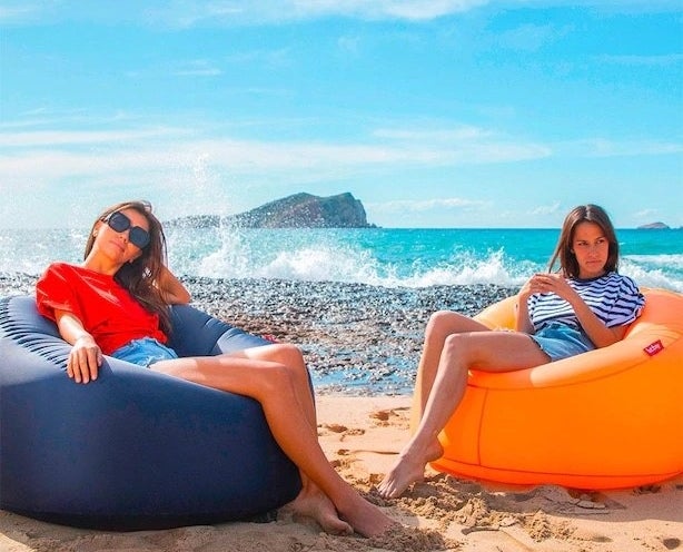 a pair of people sitting in the inflatable lounge chairs at the beach