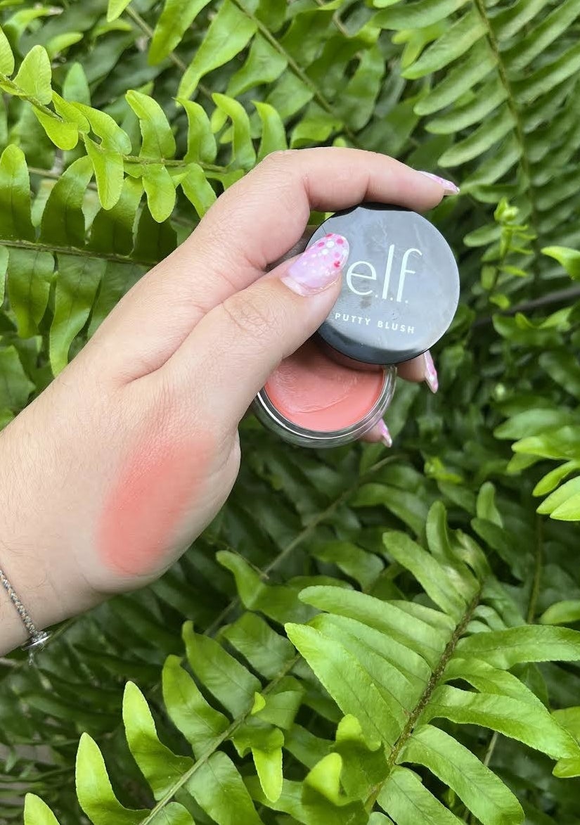 Bianca holding up the blush with a swatch on her hand in front of a plant