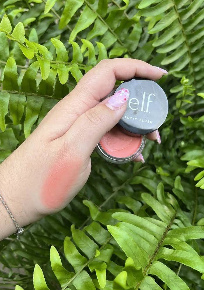 Bianca holding up the blush with a swatch on her hand in front of a plant
