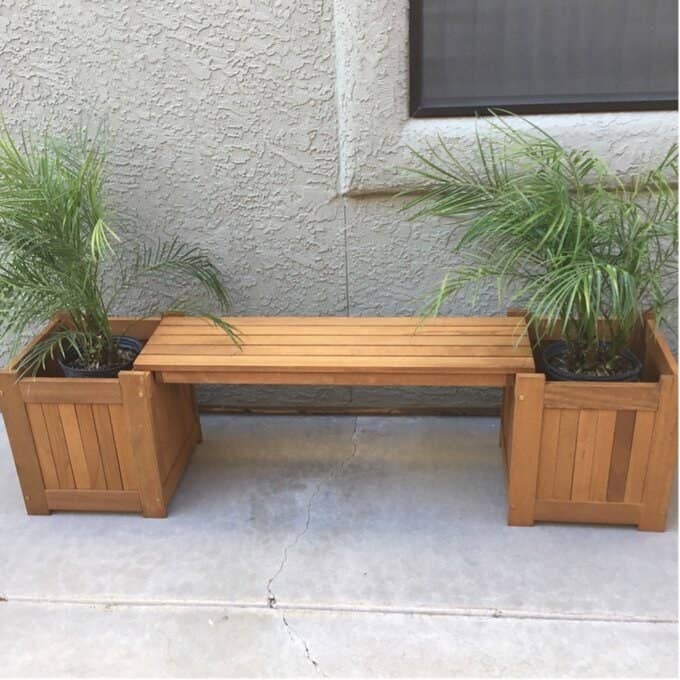 A wooden bench with two planters on both sides