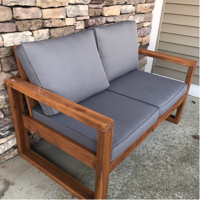 A wood-framed outdoor love seat with grey couch cushions