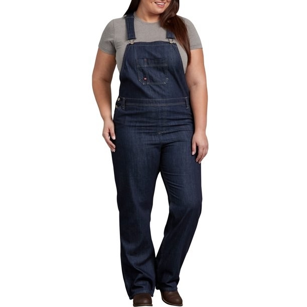 Model wearing dark blue overalls with brown shoes and grey shirt