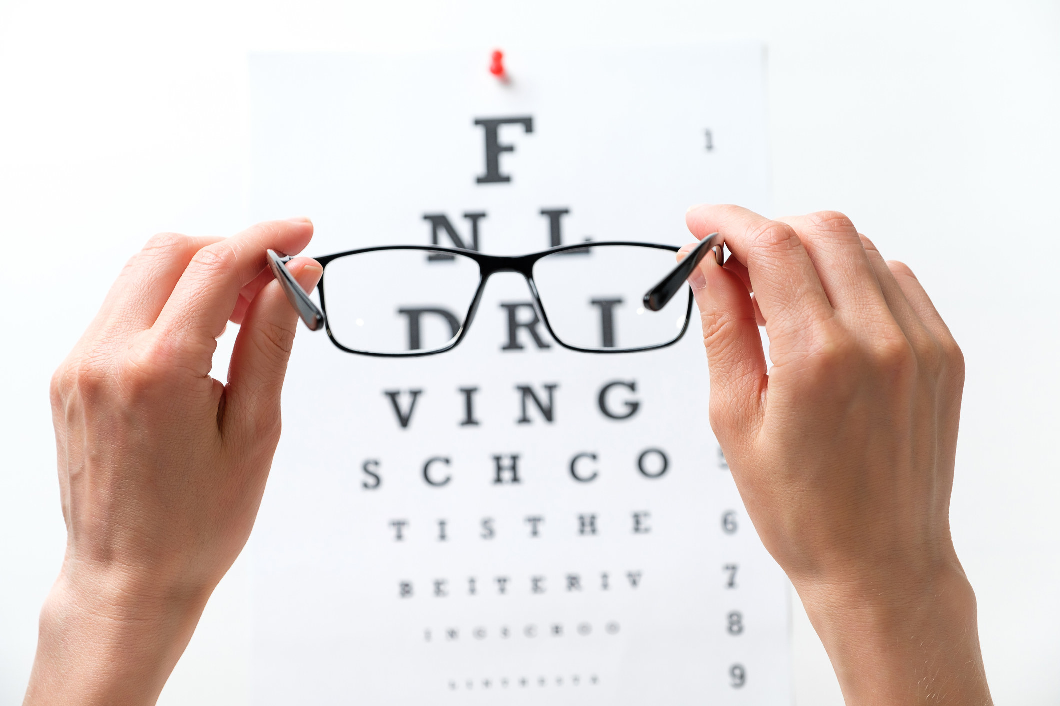 An eye test and a person&#x27;s hands holding up a pair of glasses