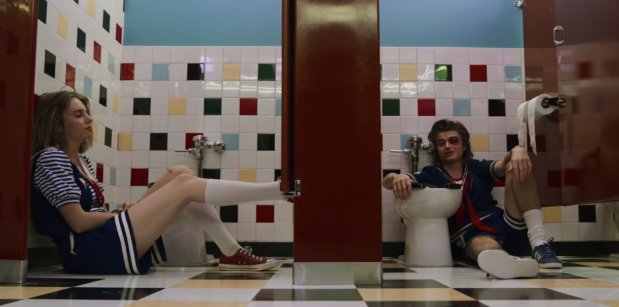two characters sitting on the floor of the bathroom in different stalls