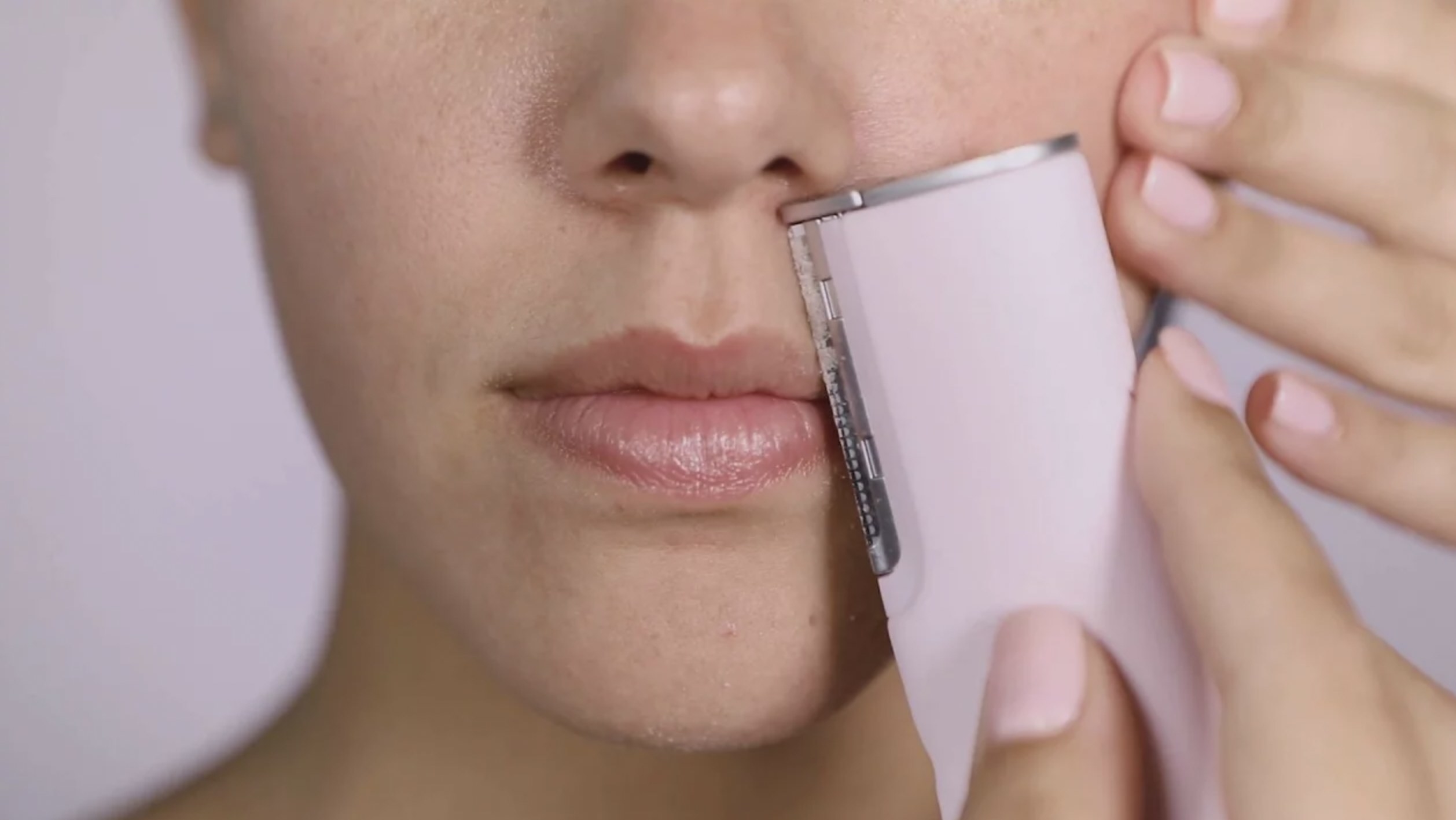 Model using the dermaplaning device to shave away peach fuzz above lip