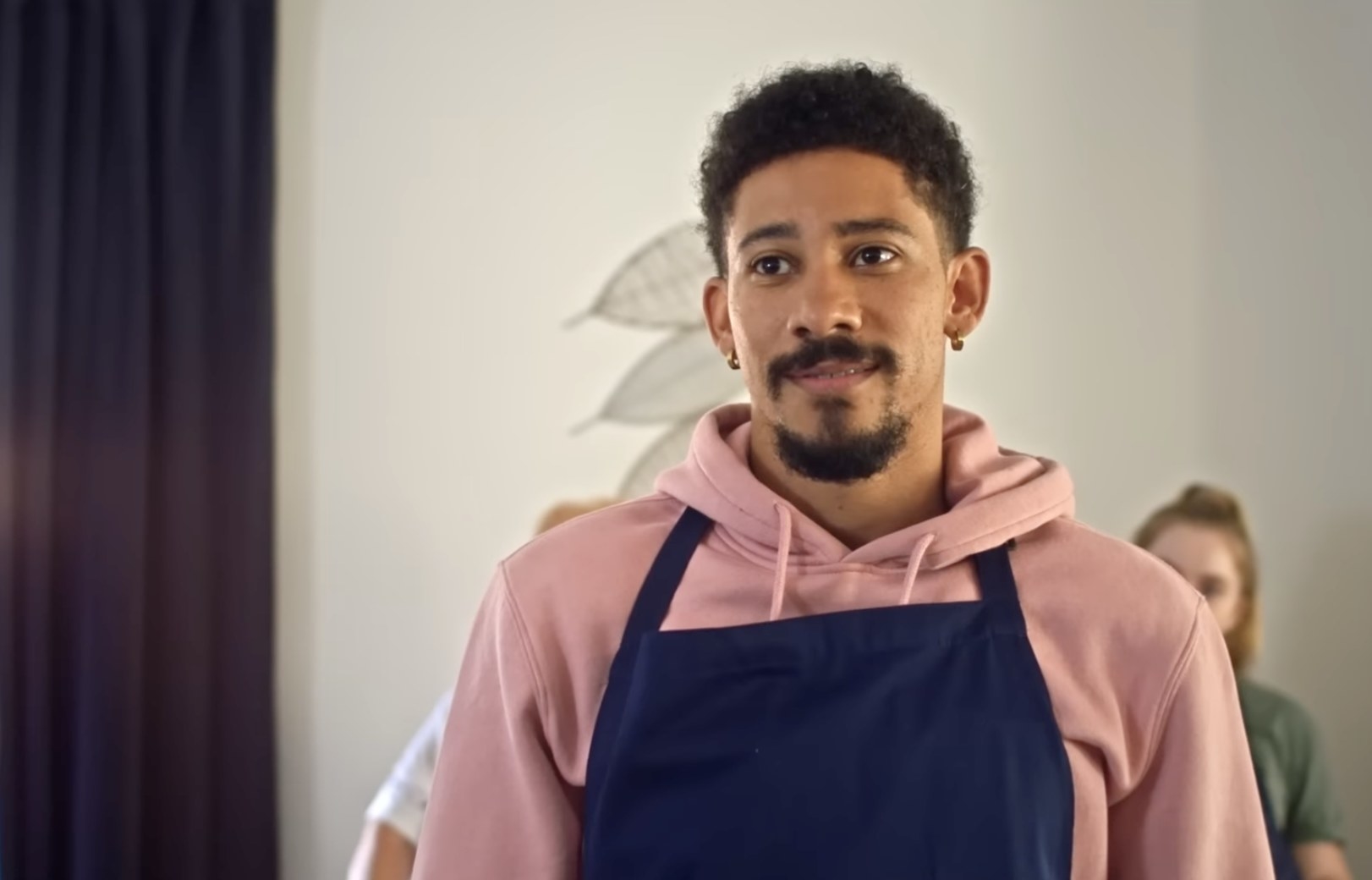 close up of Keiynan as Andrew wearing an apron over a hoodie