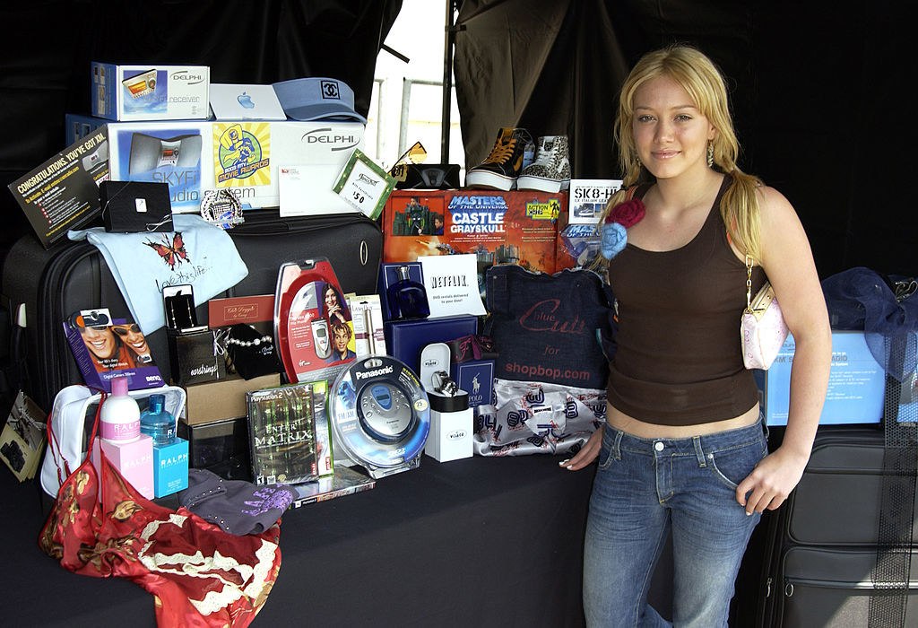 Hilary in jeans and a tank top next to an array of items, including a portable CD player