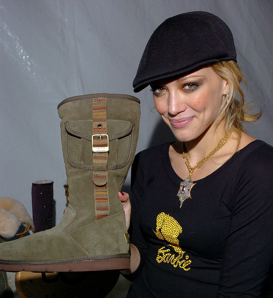 Barbie holding up a suede calf-high boot with side pocket and strap