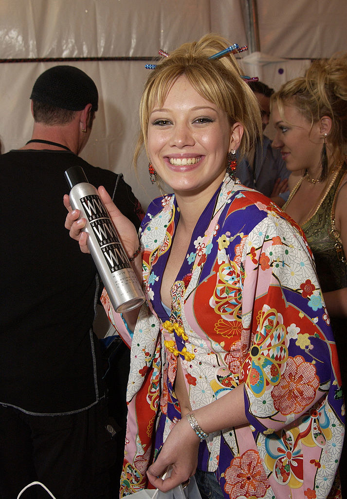Hilary smiling and holding a bottle of hairspray