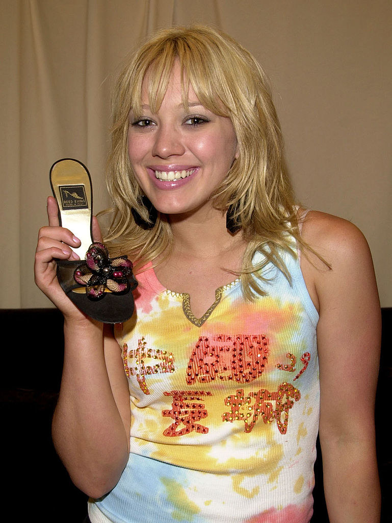 Hilary smiling and holding up a bejeweled slide sandal