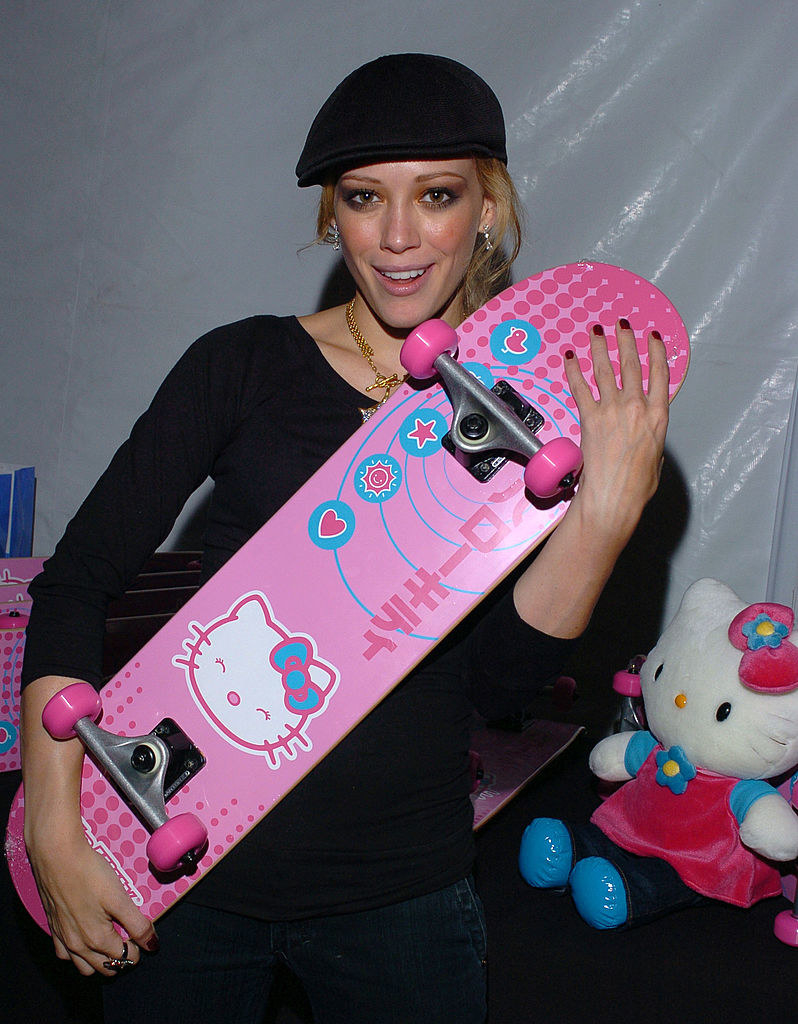 Hilary in a cap and holding a Hello Kitty skateboard
