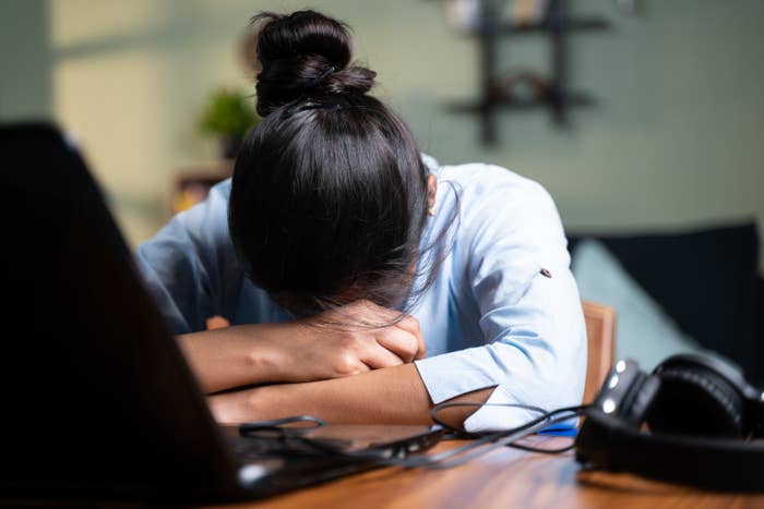 A woman with her head down at her desk feeling physically and emotionally exhausted