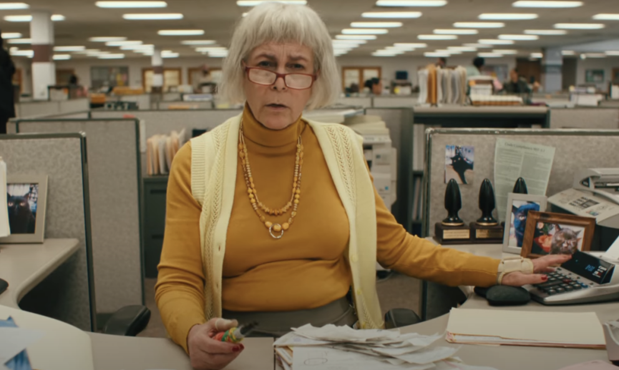 Jamie Lee Curtis as Deirdre, sitting at her desk looking down her glasses