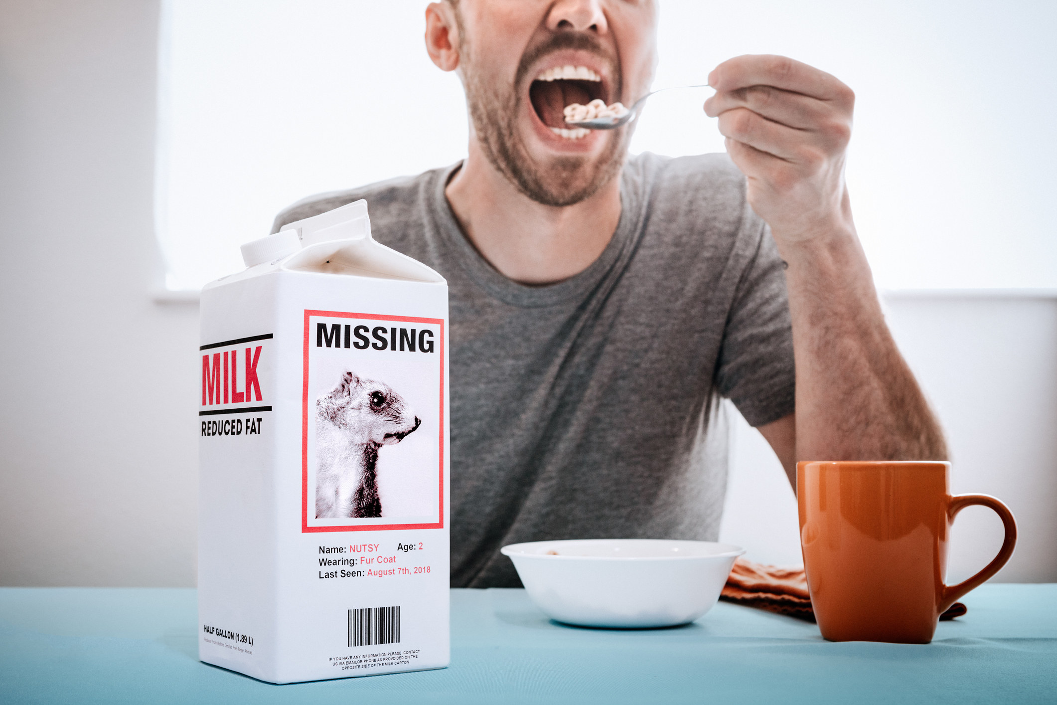 A man eating a bowl of cereal next to a carton of milk on the table with a &quot;Missing&quot; poster on the carton