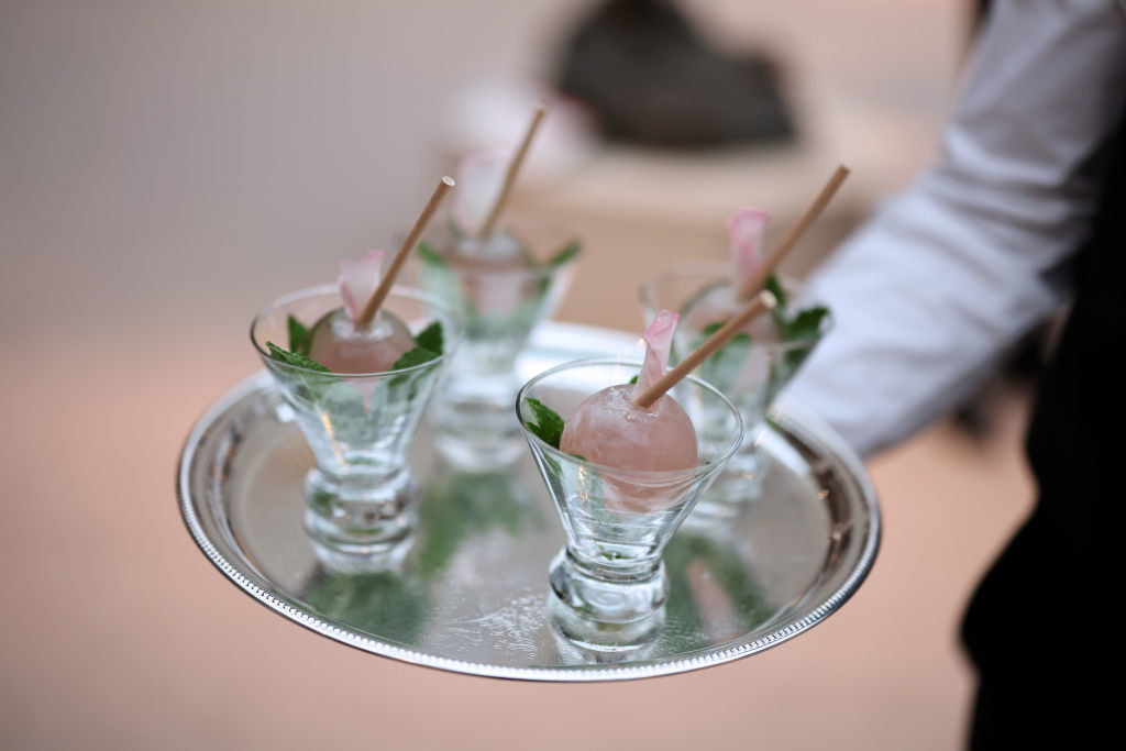 A waiter holds a tray with four small glasses with a jelly-like ball inside