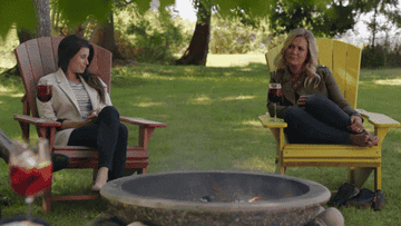 GIF of two actors sitting next to a fire pit with glasses of wine in the show &quot;Chesapeake Shores&quot;