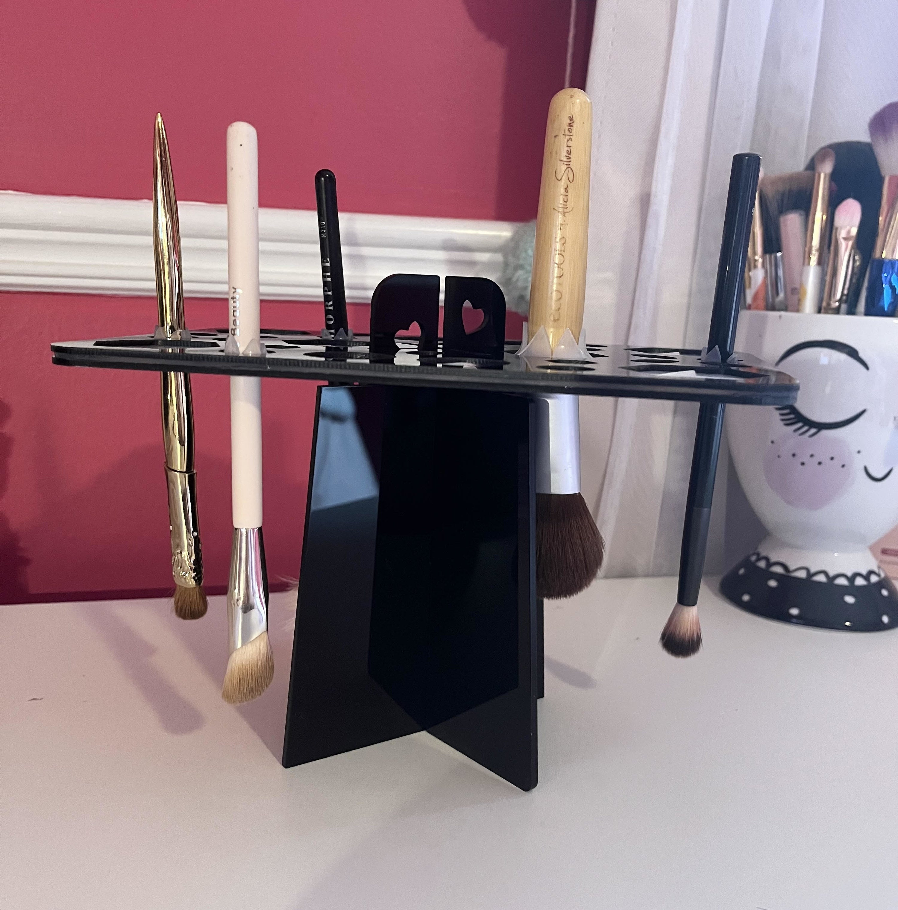 Brushes hanging in the brush holder on a table beside a cup of makeup brushes