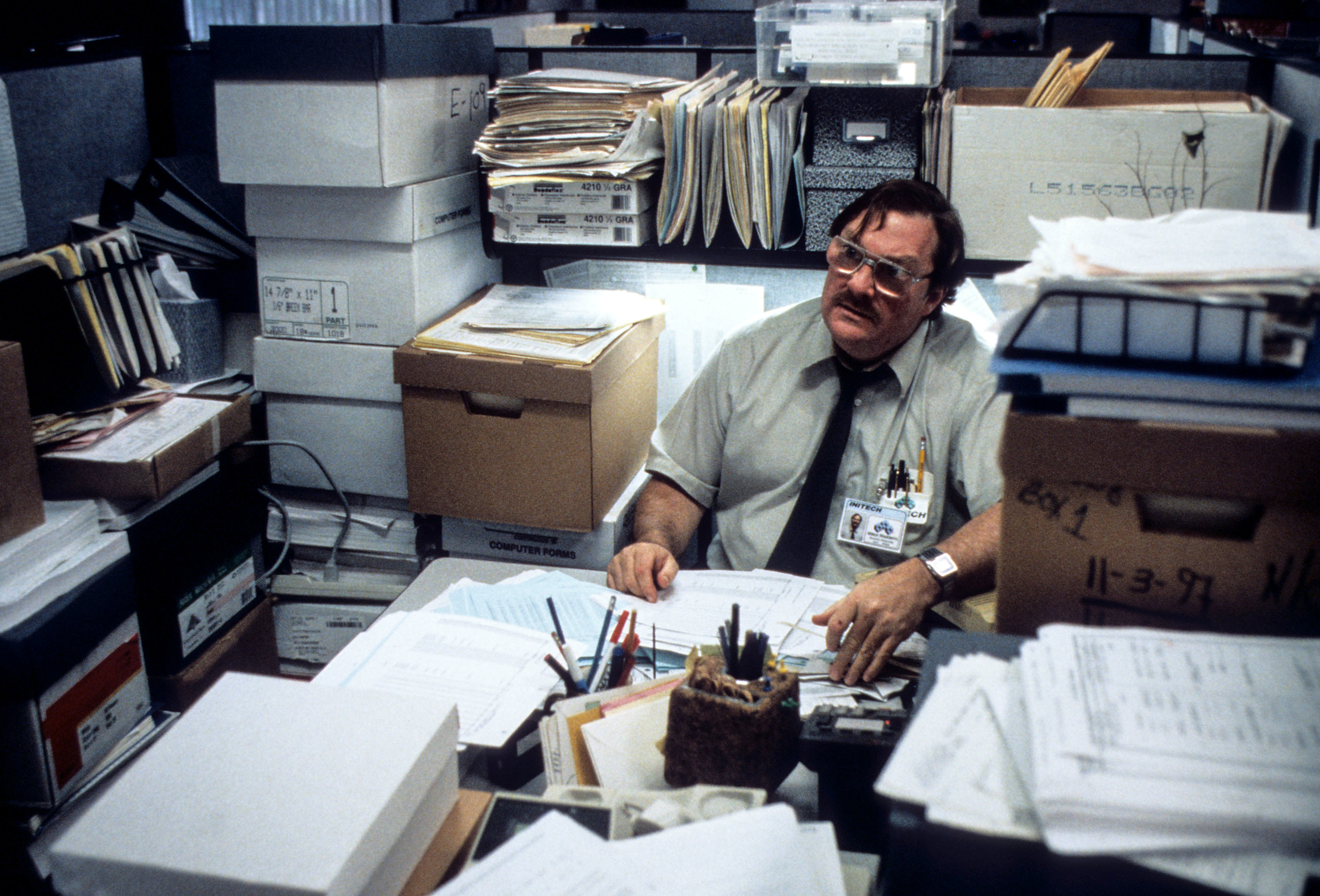 Stephen Root sits in a cubicle