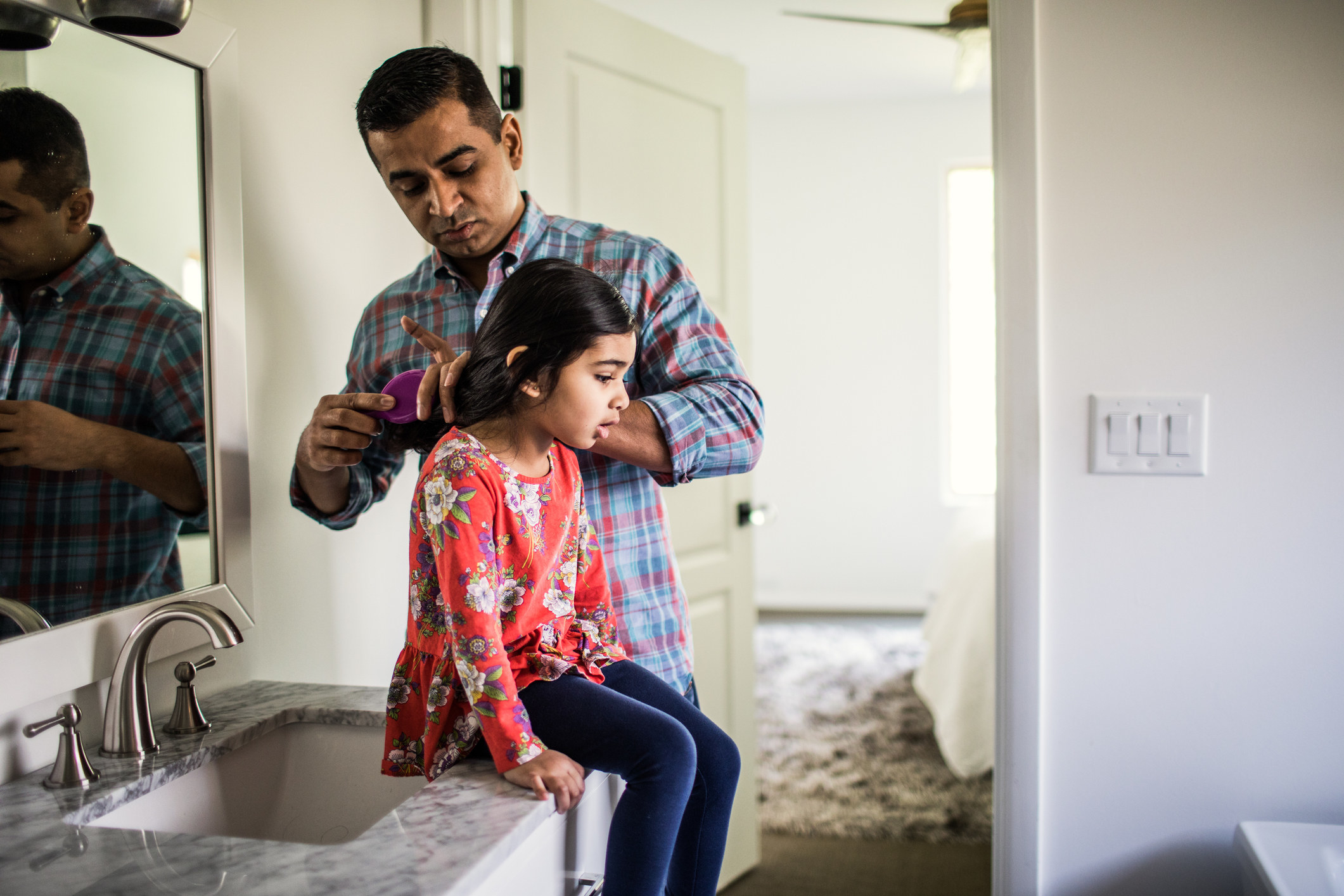 A father fixes his daughter&#x27;s hair in the bathroom.