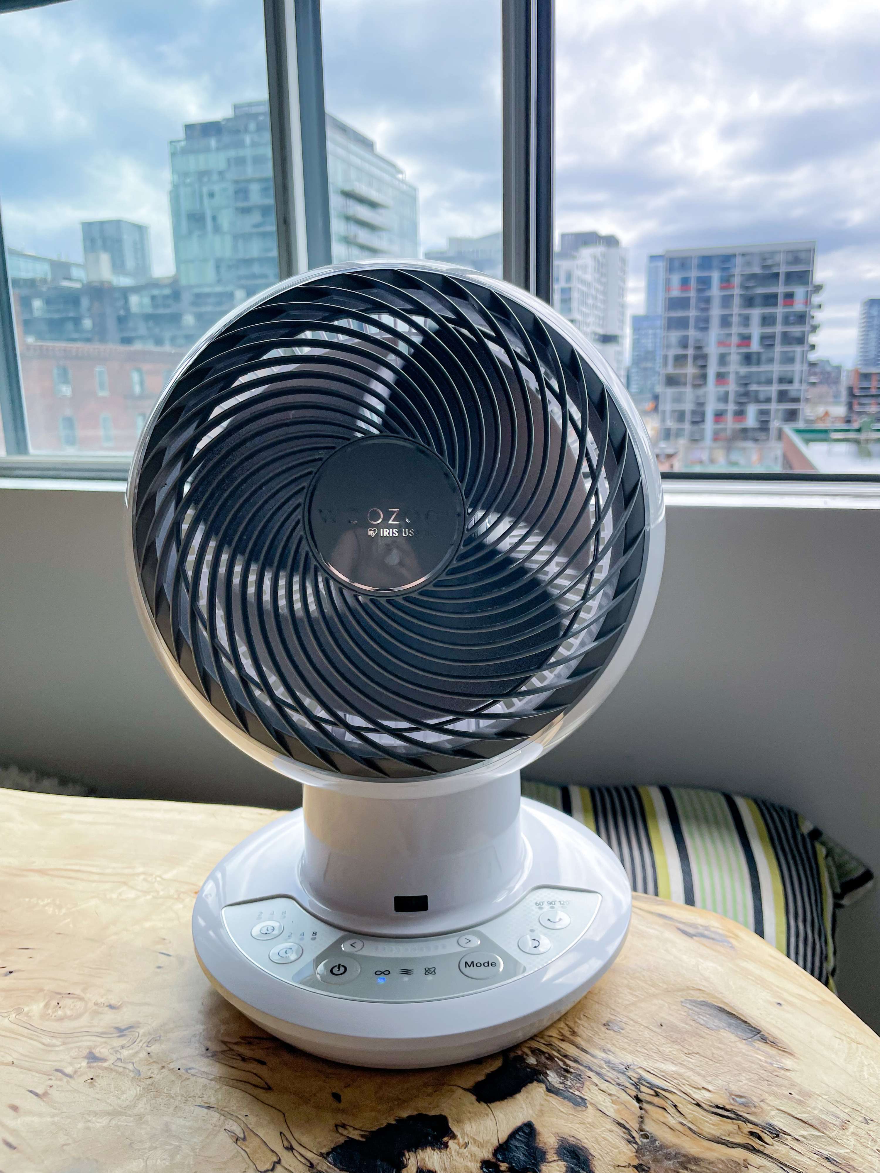 the circular oscillating fan placed on a wooden tabletop with a window visible in the background