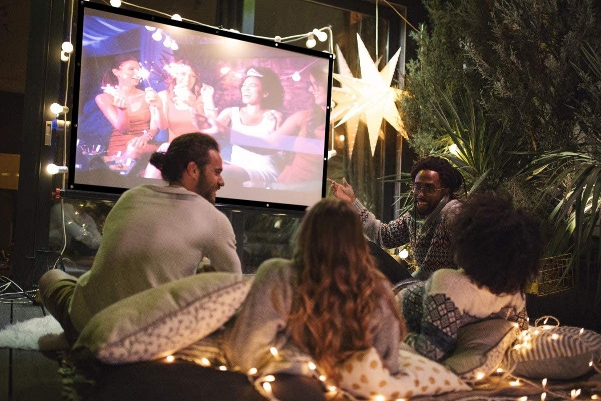 a group of people sitting outside watching a projector screen