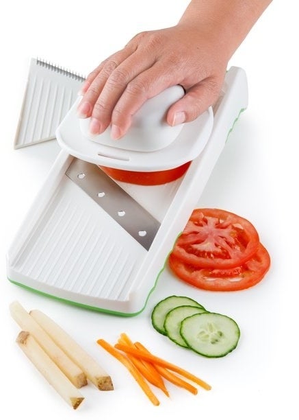 a person slicing cucumber, potatoes, and carrots with a mandolin