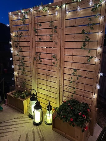 vines and lights hanging from the privacy screen with lanterns in from of it