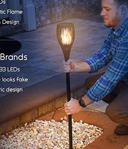 A person putting the torch lamp into the ground in a garden