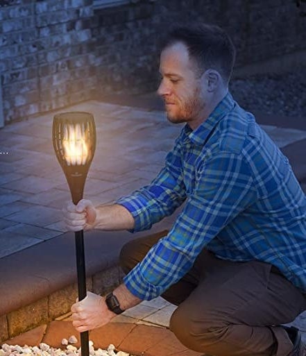 A person putting the torch lamp into the ground in a garden